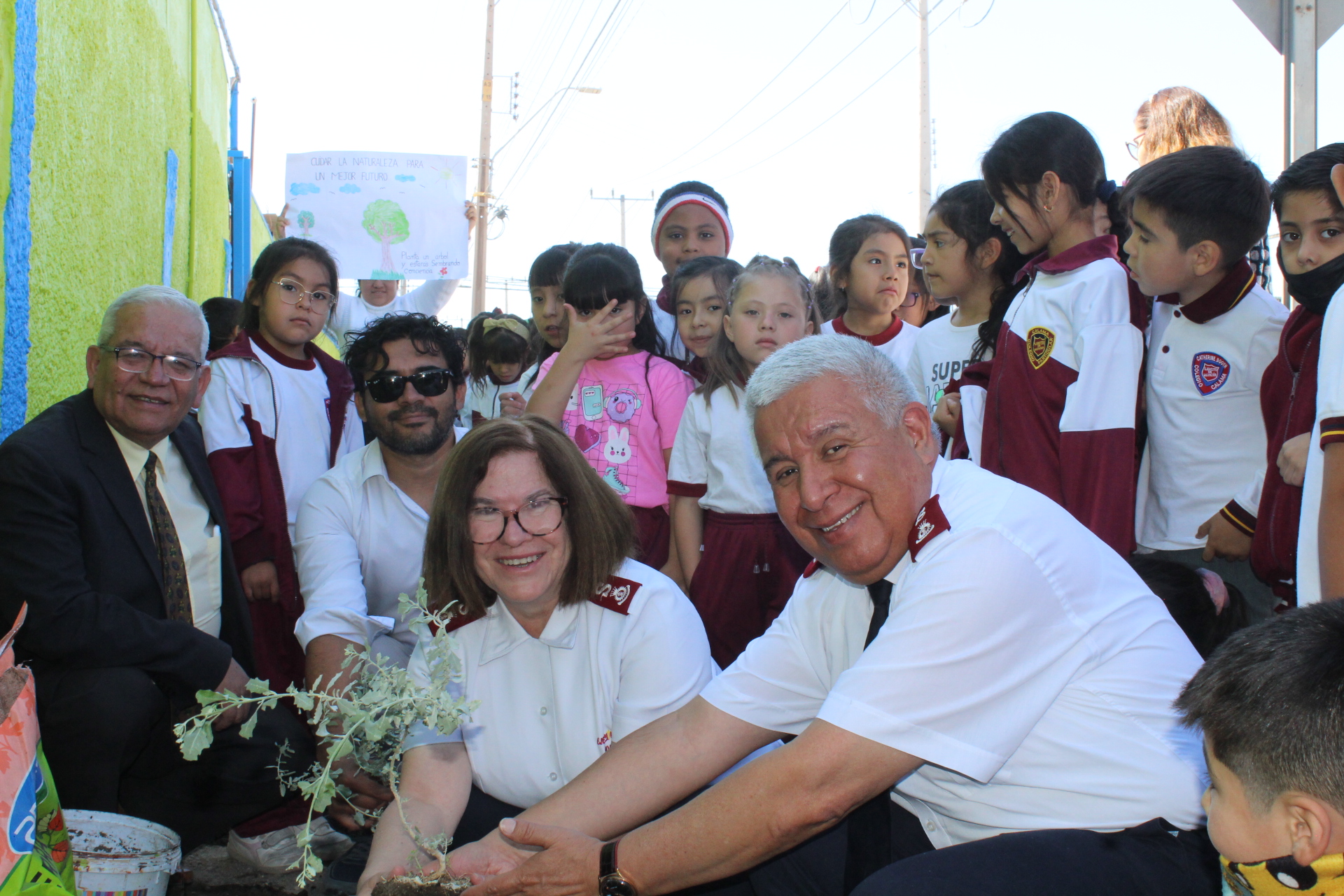 Representantes de CChC Calama y autoridades del Colegio Catherine Booth, posan mientras plantan un arbusto con niños de fondo